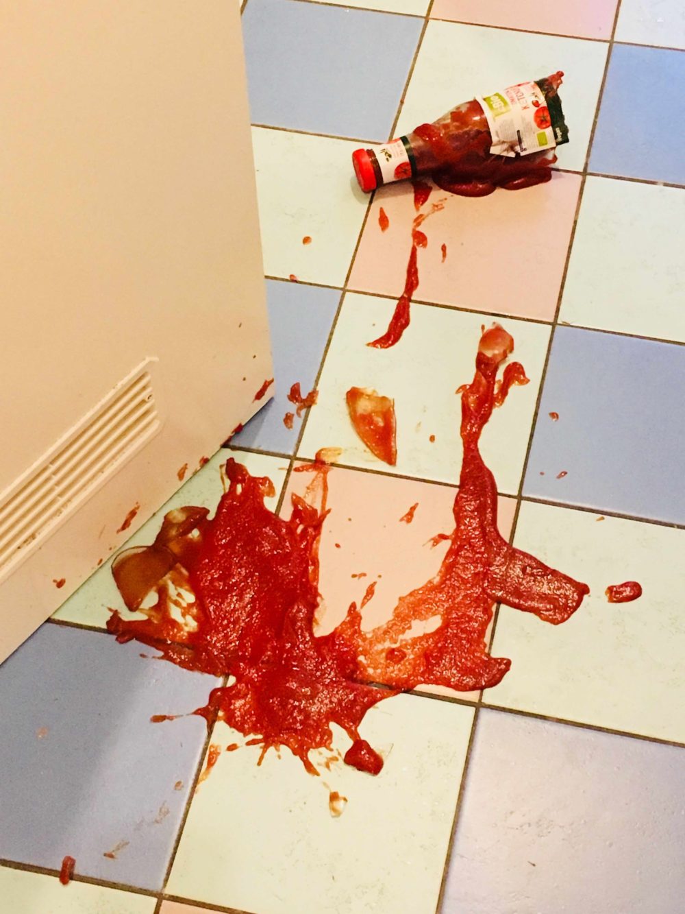 eine Ketchupflasche ist zerbrochen, der Ketchup verteilt sich auf pastellfarbenen Fliesen